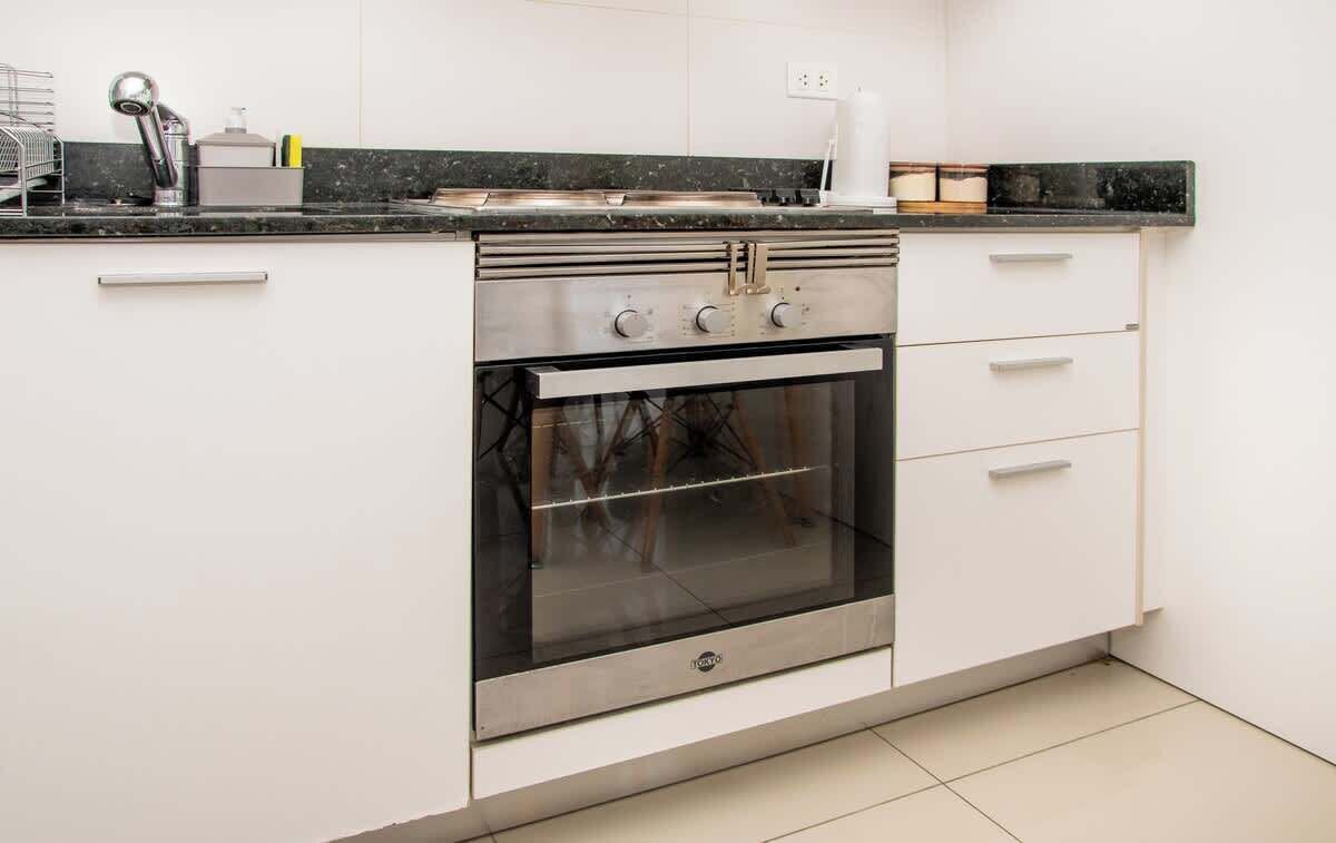 Een keuken met een ingebouwde oven, witte kastjes en een zwart aanrecht.