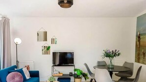 Uma sala de estar moderna com sofá, televisão, mesa de jantar, cadeiras e objetos decorativos.