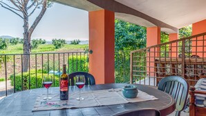 Ein Tisch mit einer Weinflasche, zwei Gläsern und einer Schale auf einem Balkon mit Blick auf Grünflächen und Hügel.