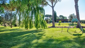 A park with trees, a swing set, and a building in the background. - Nice apartment in Roccastrada with swimming pool (Roccastrada)