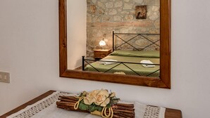 Un dormitorio con pared de piedra, estructura de cama de madera, mesita de noche con lámpara y un espejo.
