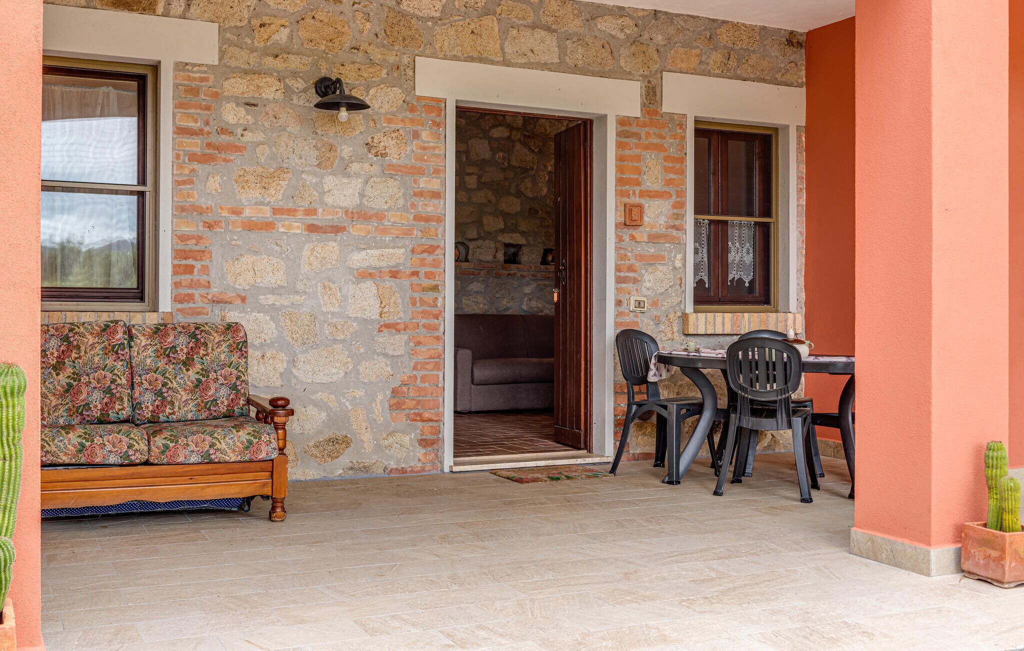 A stone building with a wooden bench, a table with chairs, and a doorway leading to an interior space.