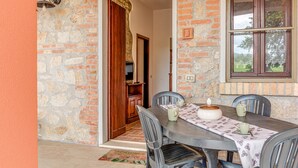 Una habitación con paredes de piedra, una puerta de madera, una mesa con sillas y una ventana con cortina de encaje.