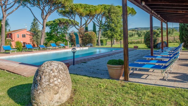 Un área de piscina con sillas de descanso, una pérgola y una estructura de piedra.