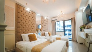 Hotellihuone, jossa on suuri sänky, pienempi sänky, televisio, työpöytä ja suuri ikkuna.