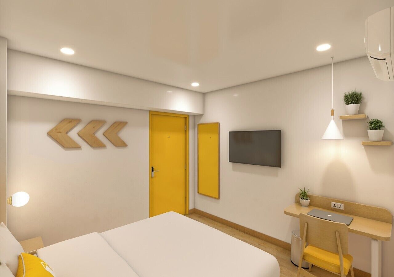 Habitación de hotel con cama, escritorio, silla, televisor y una puerta amarilla.