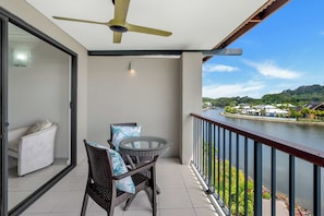 Ein Balkon mit einem Glastisch und Korbstühlen, mit Blick auf einen Fluss und ein Wohngebiet.