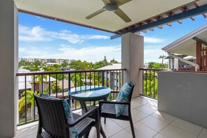 A balcony with a table and chairs, a ceiling fan, and a view of buildings and greenery. - Bluewater Hideaway—Lagoon Outlook by Trinity Beach (Trinity Beach)