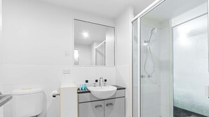 A modern bathroom with a toilet, sink, mirror, and glass-enclosed shower. - Bluewater Hideaway - Lagoon Outlook by Trinity Beach (Trinity Beach)