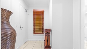 A hallway with a large vase, a wooden table, and a window with blinds. - Bluewater Hideaway - Lagoon Outlook by Trinity Beach (Trinity Beach)