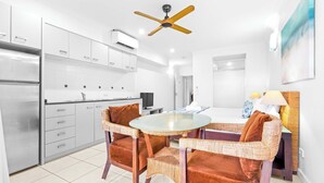 A modern kitchen with white cabinets, a stainless steel refrigerator, a round glass table, wicker chairs, and a ceiling fan. - Bluewater Hideaway - Lagoon Outlook by Trinity Beach (Trinity Beach)