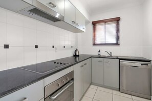 A modern kitchen with a black countertop, stainless steel appliances, and a window with blinds. - Bluewater Haven - Sweeping Lagoon Views with Pool (Trinity Beach)