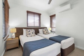 Une chambre d’hôtel avec deux lits, une table de chevet, une lampe et un ventilateur de plafond.