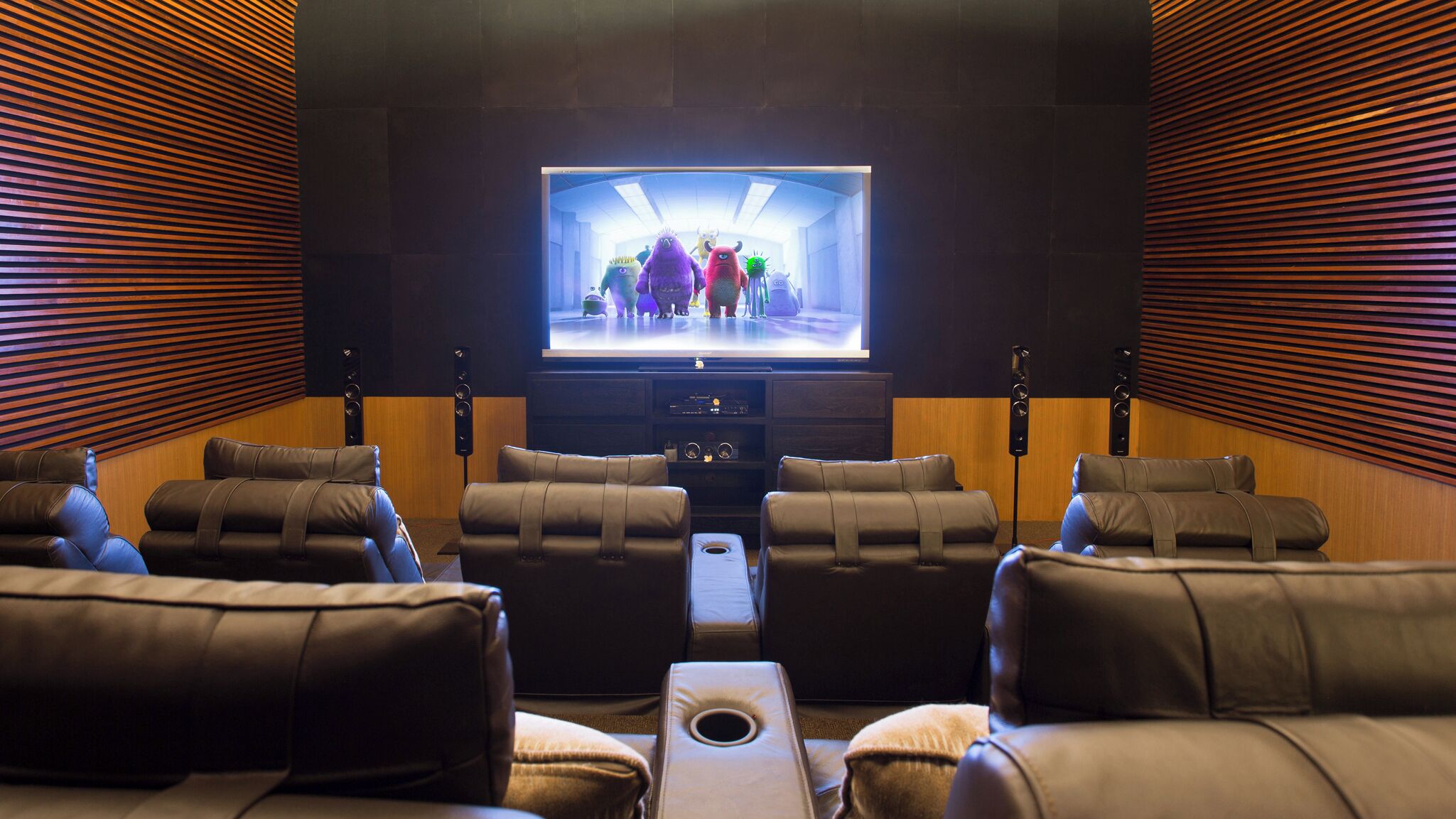 Un cine en casa con sillones de cuero reclinables, un televisor de pantalla plana grande y paneles de madera.