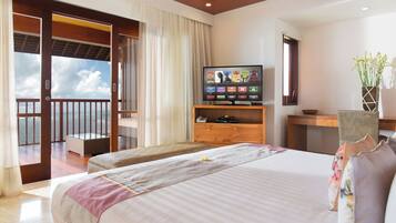 A hotel room with a large bed, a TV on a wooden stand, a desk, and a view of the ocean through a sliding door.