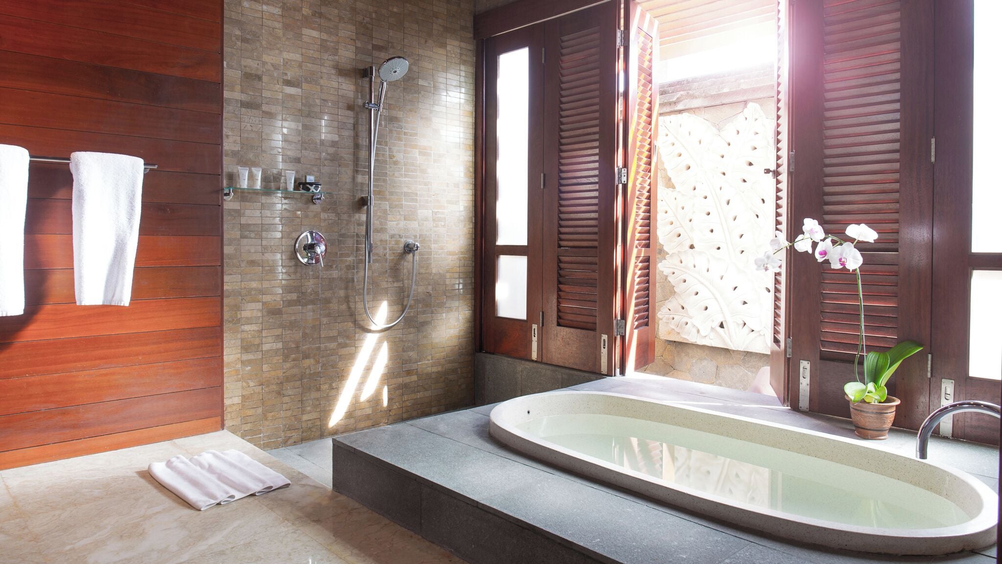 Un baño moderno con una bañera independiente, ducha y una orquídea en maceta.