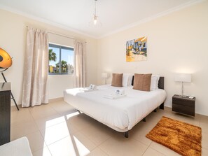 A hotel room with a large bed, a desk with a lamp, a painting on the wall, and a window with curtains. - Pool and Large Balcony by Lagos Marina (Lagos)