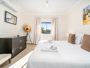 Une chambre d’hôtel avec un lit, un bureau, une lampe, un tableau et une fenêtre avec des rideaux.