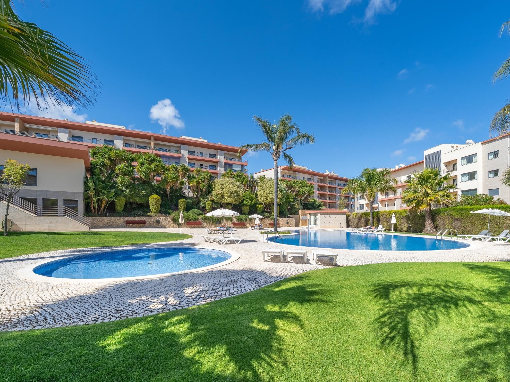 A resort with a swimming pool, lounge chairs, and a building with balconies.