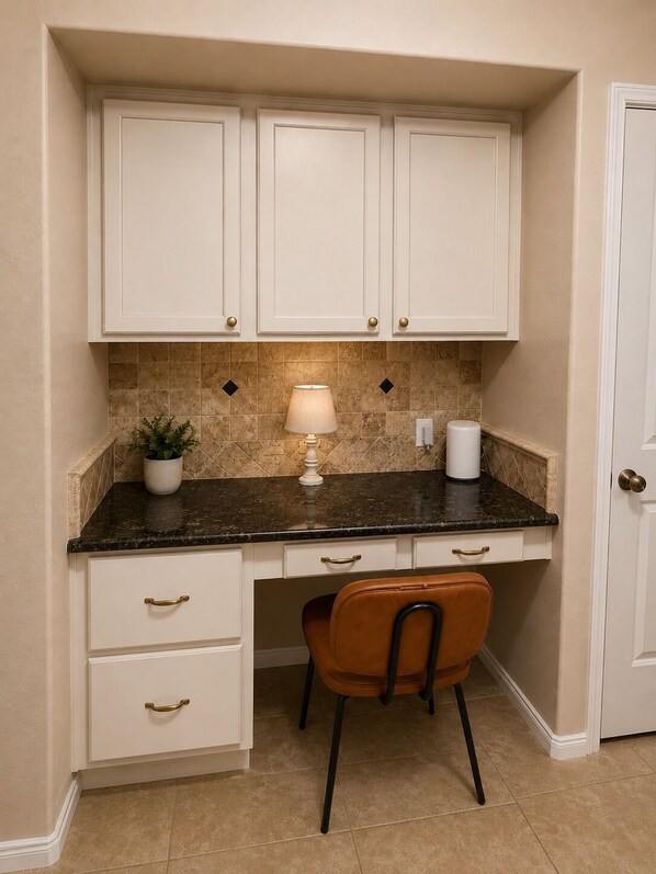 A compact kitchen with white cabinets, a dark countertop, a single chair, and a potted plant.