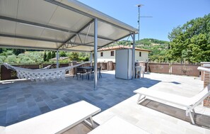 Une terrasse extérieure couverte, équipée d’un hamac, d’une table et de chaises.