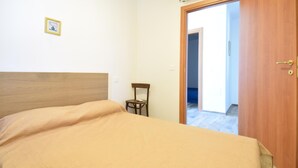 Un dormitorio con una cama, una silla, una puerta y un pequeño cuadro en la pared.