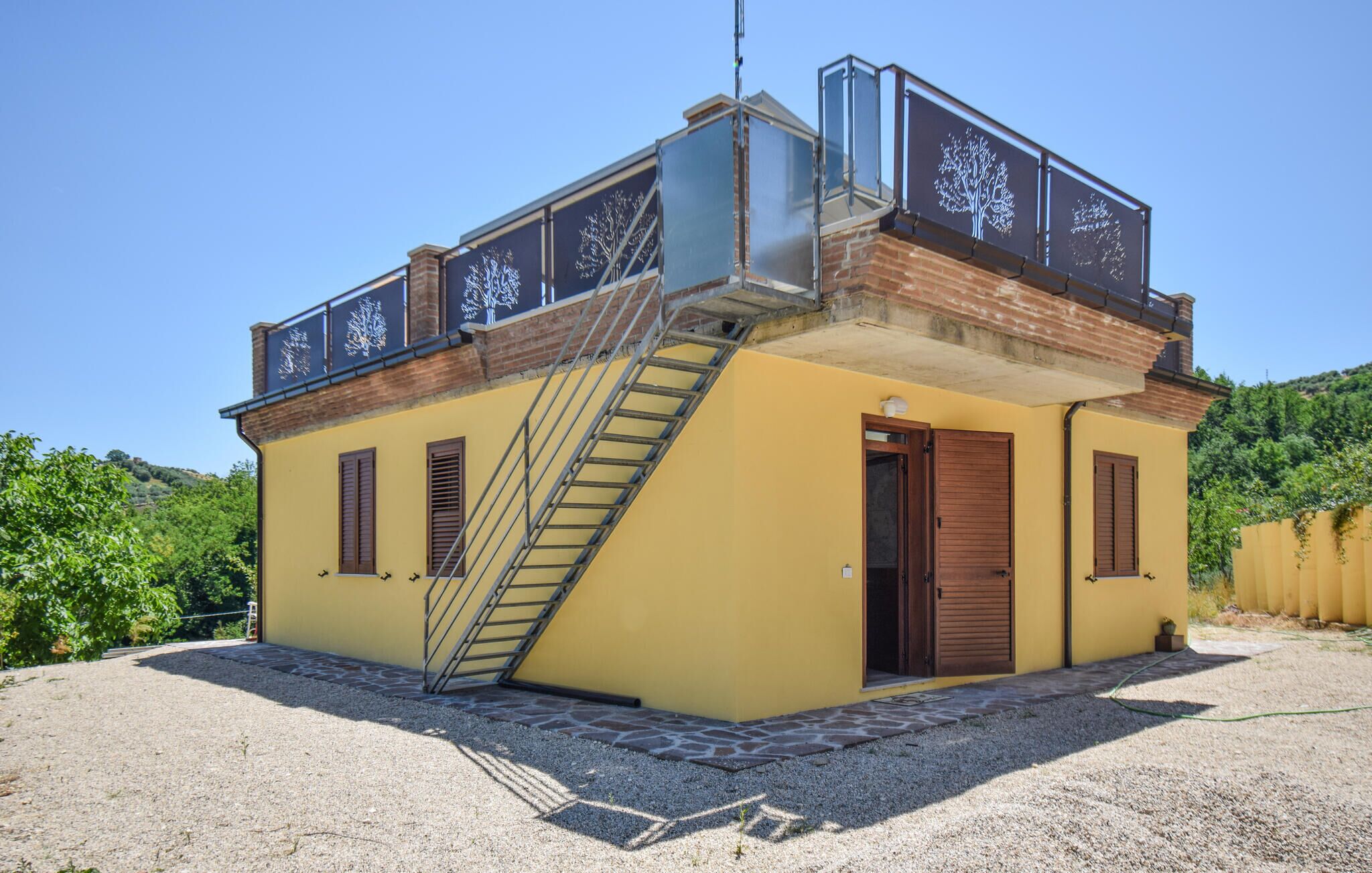 A two-story building with a yellow facade, a metal staircase, and a balcony with tree designs.