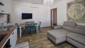 Una sala de estar con sofá, una mesa de comedor con sillas, un televisor montado en la pared y un mapa en la pared.