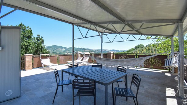 Un patio techado con mesa y sillas, una hamaca y vistas a las colinas.
