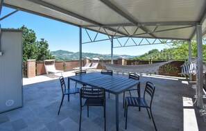 Une terrasse couverte avec une table et des chaises, un hamac et une vue sur les collines.