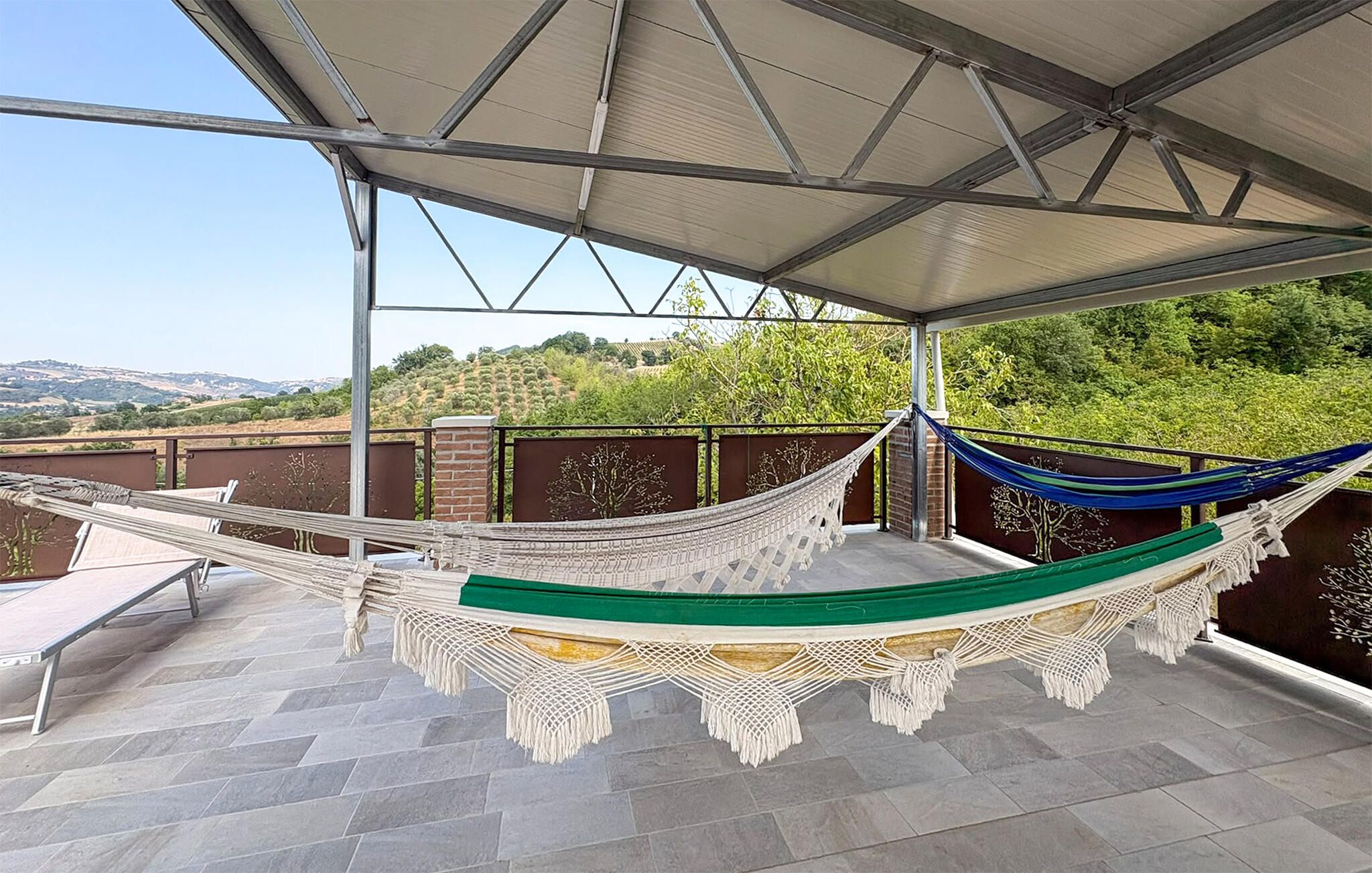 A hammock under a covered patio with a view of a hilly landscape.
