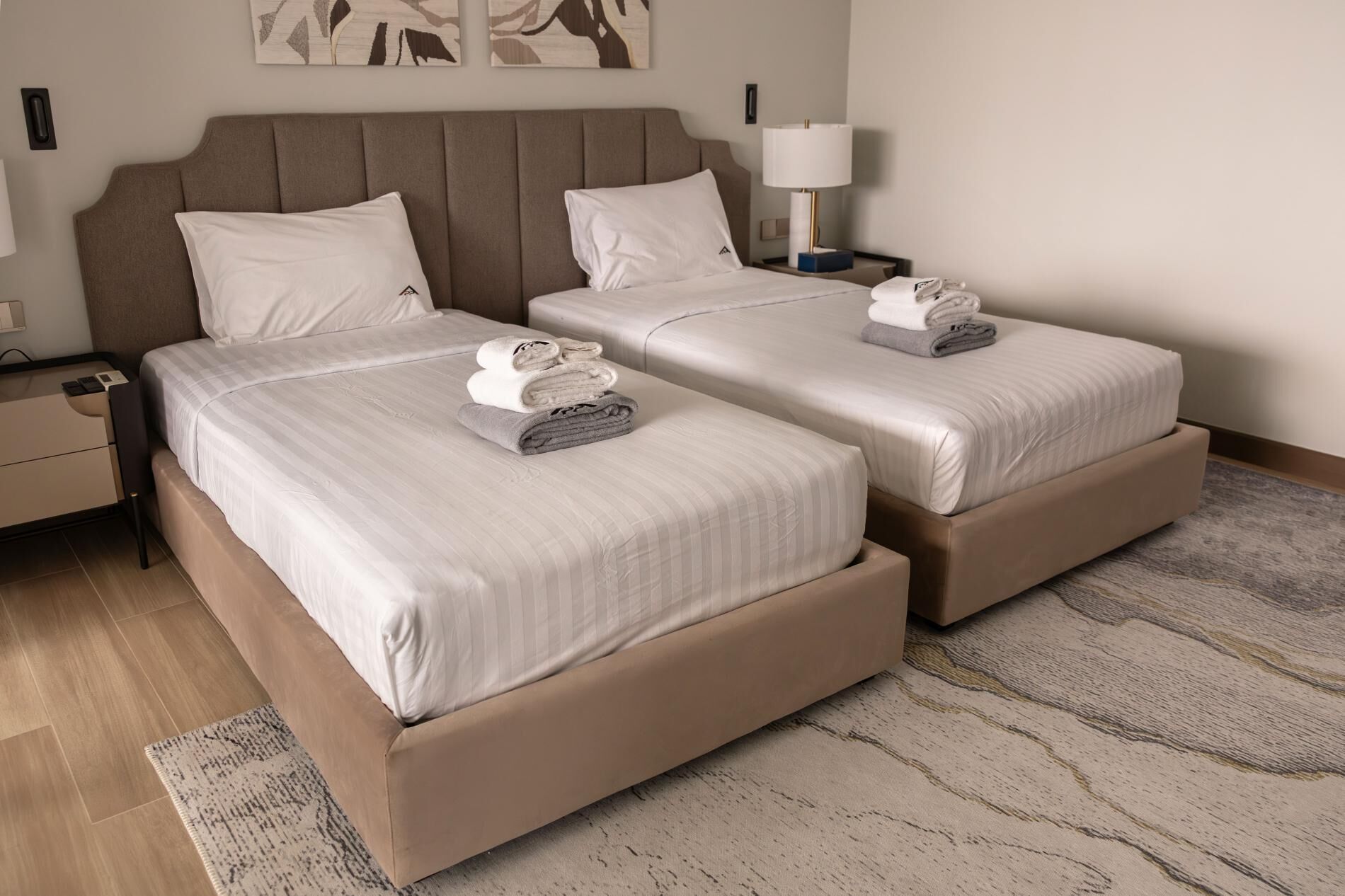 A hotel room with two beds, a nightstand with a lamp, and a wall-mounted artwork.
