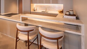 A modern kitchen with a marble countertop, built-in cabinets, a sink, and two bar stools. - The Angsana Oceanview Residences Unit 235 (Choeng Thale)