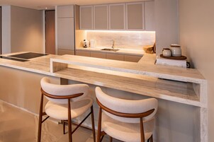 A modern kitchen with a marble countertop, built-in cabinets, a sink, and two bar stools.