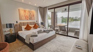 A modern hotel room with a large bed, a balcony with a table and chairs, and a view of a body of water. - The Angsana Oceanview Residences Unit 235 (Choeng Thale)