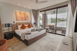 Una habitación de hotel moderna con una cama grande, un balcón con mesa y sillas, y vista a un cuerpo de agua.