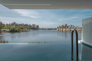 Une piscine à débordement offrant une vue sur un lac et les bâtiments du complexe hôtelier.