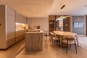 A modern kitchen with a central island, a dining area with a round table and chairs, and a living space with a TV.
