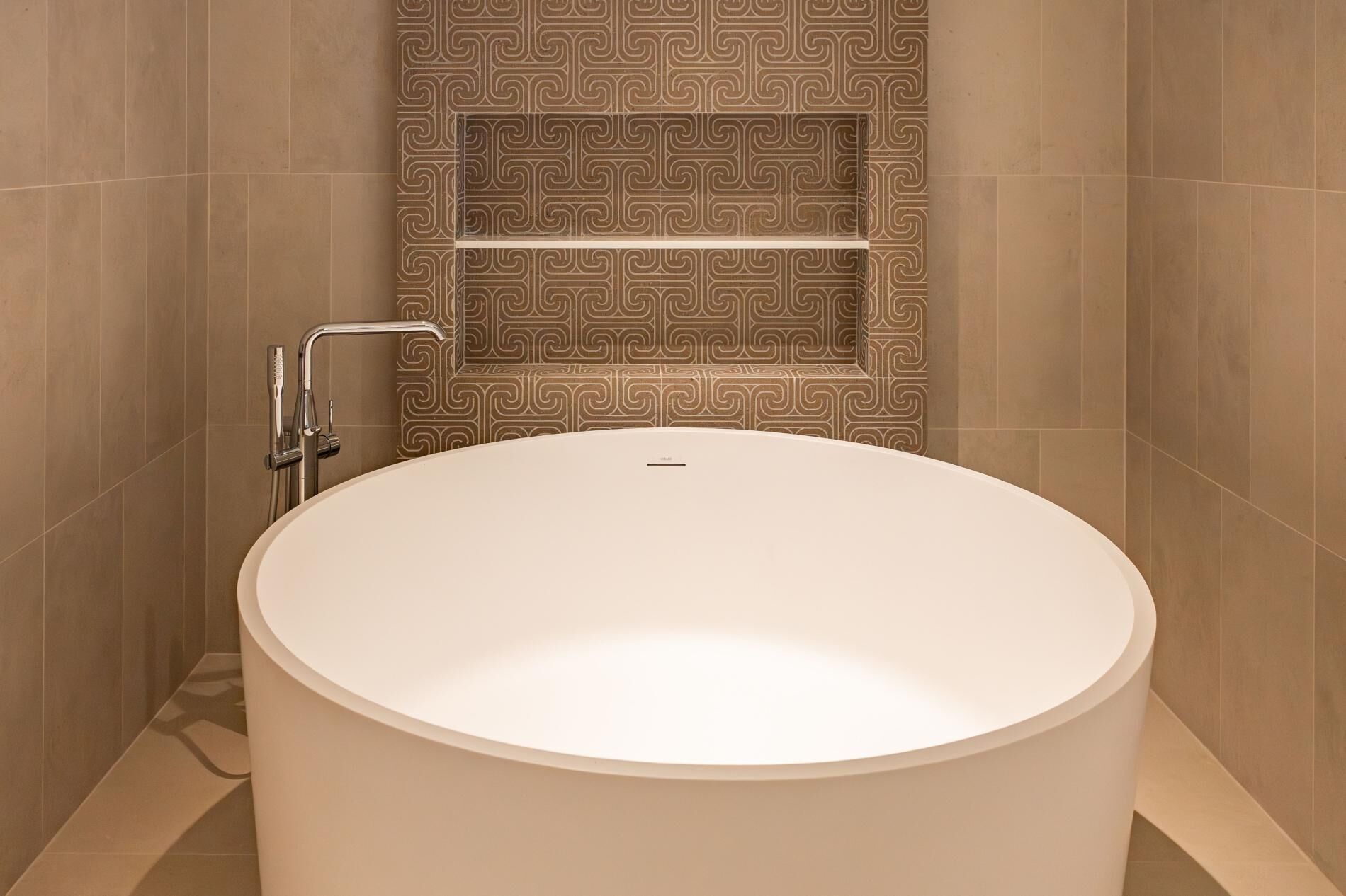 A modern bathroom with a large oval bathtub, a shower with a handheld showerhead, and a patterned wall.