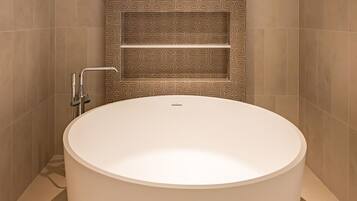 A modern bathroom with a large oval bathtub, a shower with a handheld showerhead, and a patterned wall.