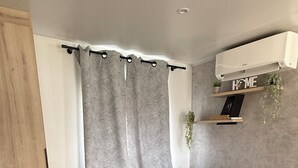 Ein modernes Schlafzimmer mit einem großen Bett, einem Kopfteil, einer Wandklimaanlage, einem Regal mit Dekoration und einem Vorhang.