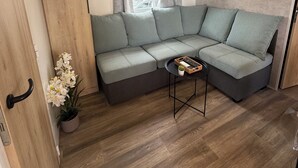 Ein modernes Wohnzimmer mit einem Ecksofa, einem kleinen Tisch, einer Topfpflanze und einem Schild mit dem Schriftzug 'HOME'.