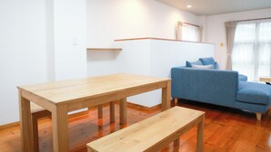Quarto com mesa de madeira, um banco, sofá azul e janela com cortinas.