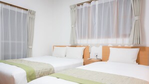 Quarto de hotel com duas camas, cabeceira de madeira, mesa de cabeceira com abajur e cortinas finas.
