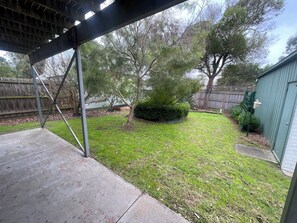 A backyard with a covered patio, a lawn, a wooden fence, and a shed.