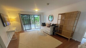 Une chambre moderne avec un grand tapis, un lit doté de rangements, une armoire en bois et une porte-fenêtre coulissante donnant sur l’extérieur.
