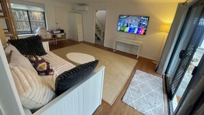 Un salon avec un canapé, un téléviseur, un escalier et une vue à travers une porte vitrée.