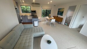 Un salon moderne avec un canapé d’angle, une petite table blanche et un coin repas comprenant des chaises et un buffet en bois.