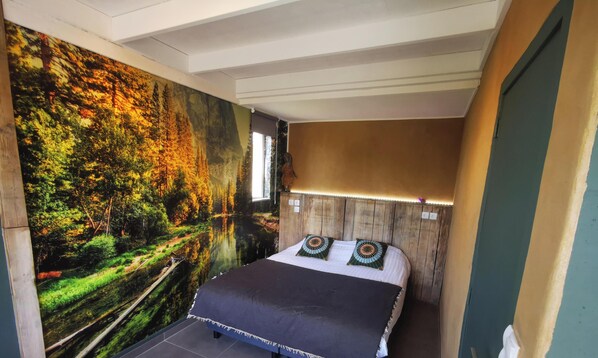 A bedroom with a large forest mural, a wooden headboard, and a bed with patterned pillows.