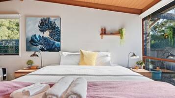 A bedroom with a bed, pillows, a painting, bedside tables with lamps, and a window with a view.